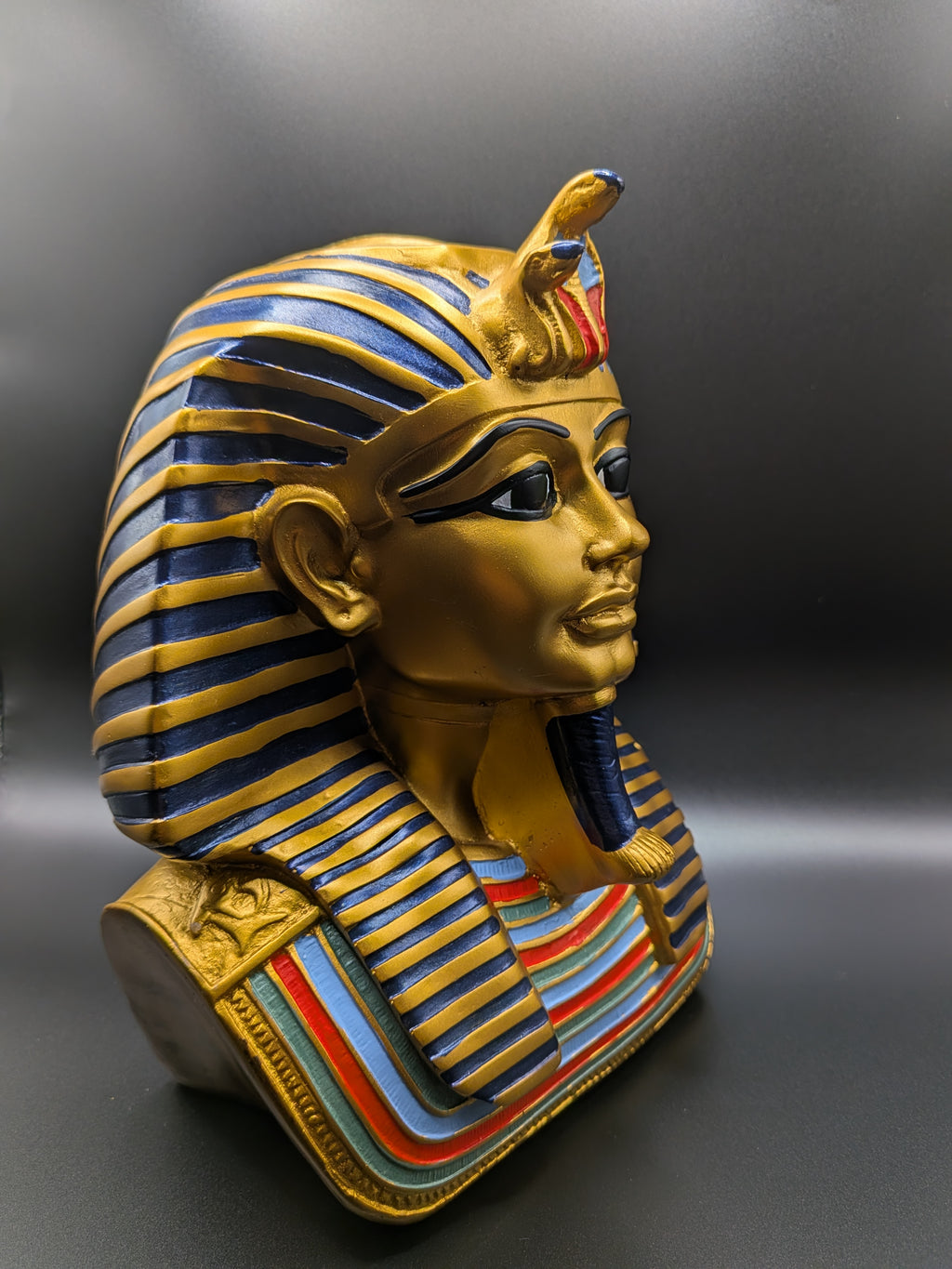 Gold Egyptian pharaoh mask with blue and red stripes on a gray background