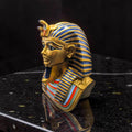 Handcrafted King Tutankhamun bust figurine in gold and blue, side profile on black reflective surface