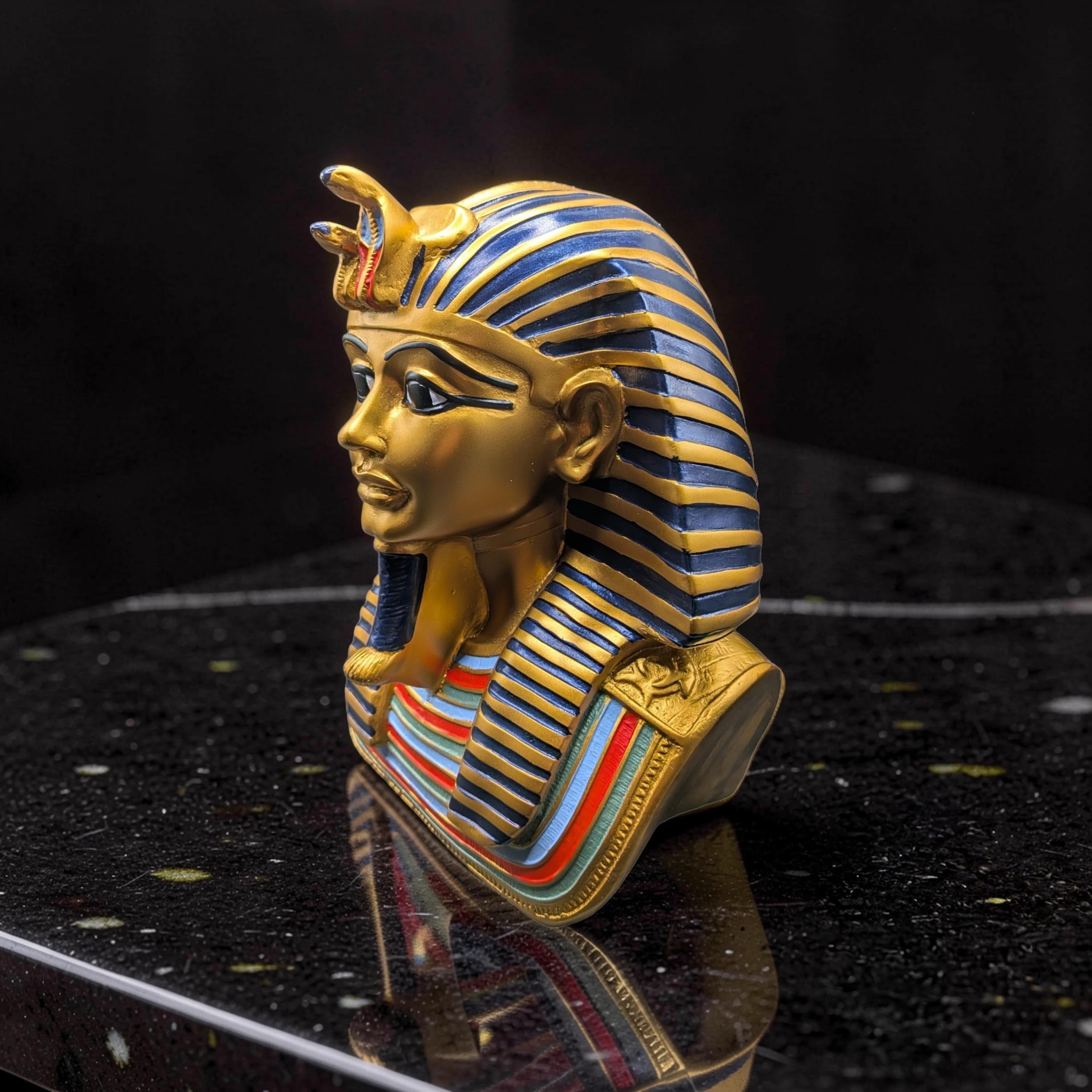 Handcrafted King Tutankhamun bust figurine in gold and blue, side profile on black reflective surface